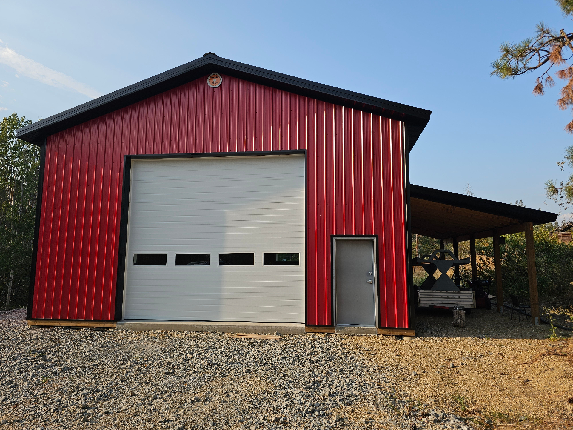 Completed red acreage shop with white roll-up door and lean-to