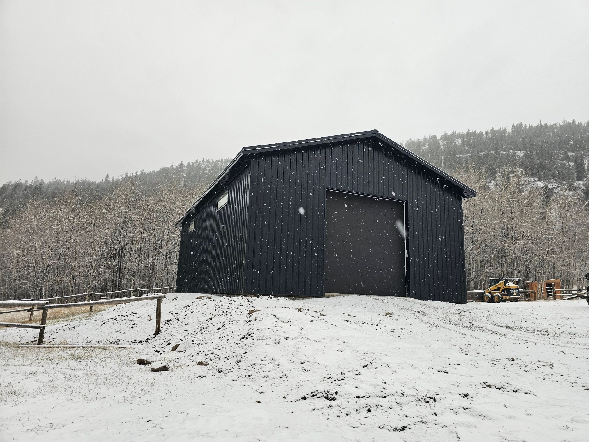 Black post frame acreage shop with roll-up door in winter snow